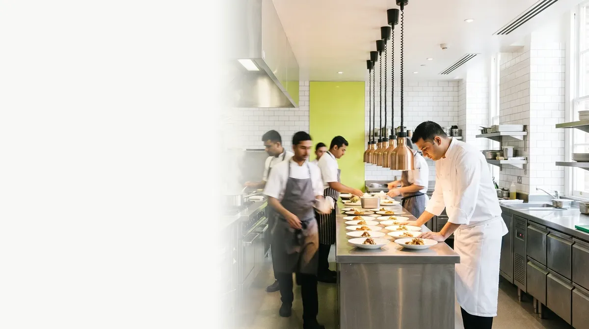 The pass in a hotel kitchen before service: cooks plating under copper lamps